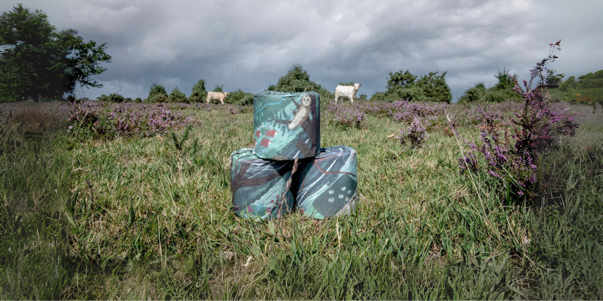 decorative toilet rolls stacked in landscape with cows in background