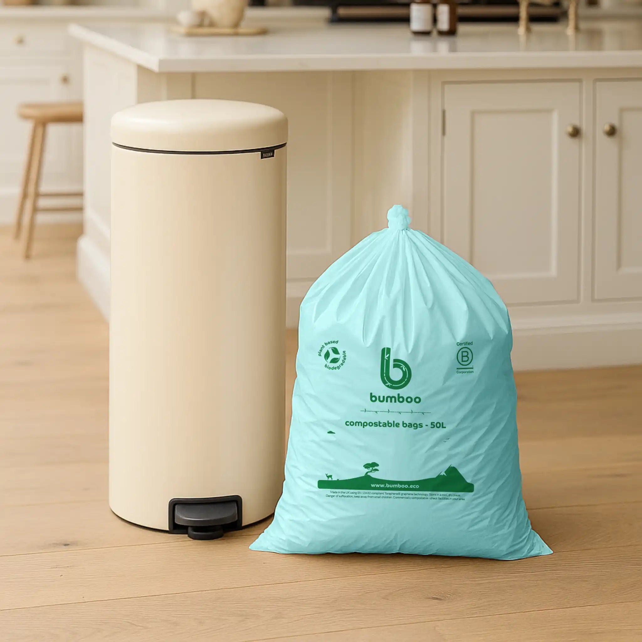 Beige trash bin with a bag of compostable bags on a wooden floor in a kitchen setting.