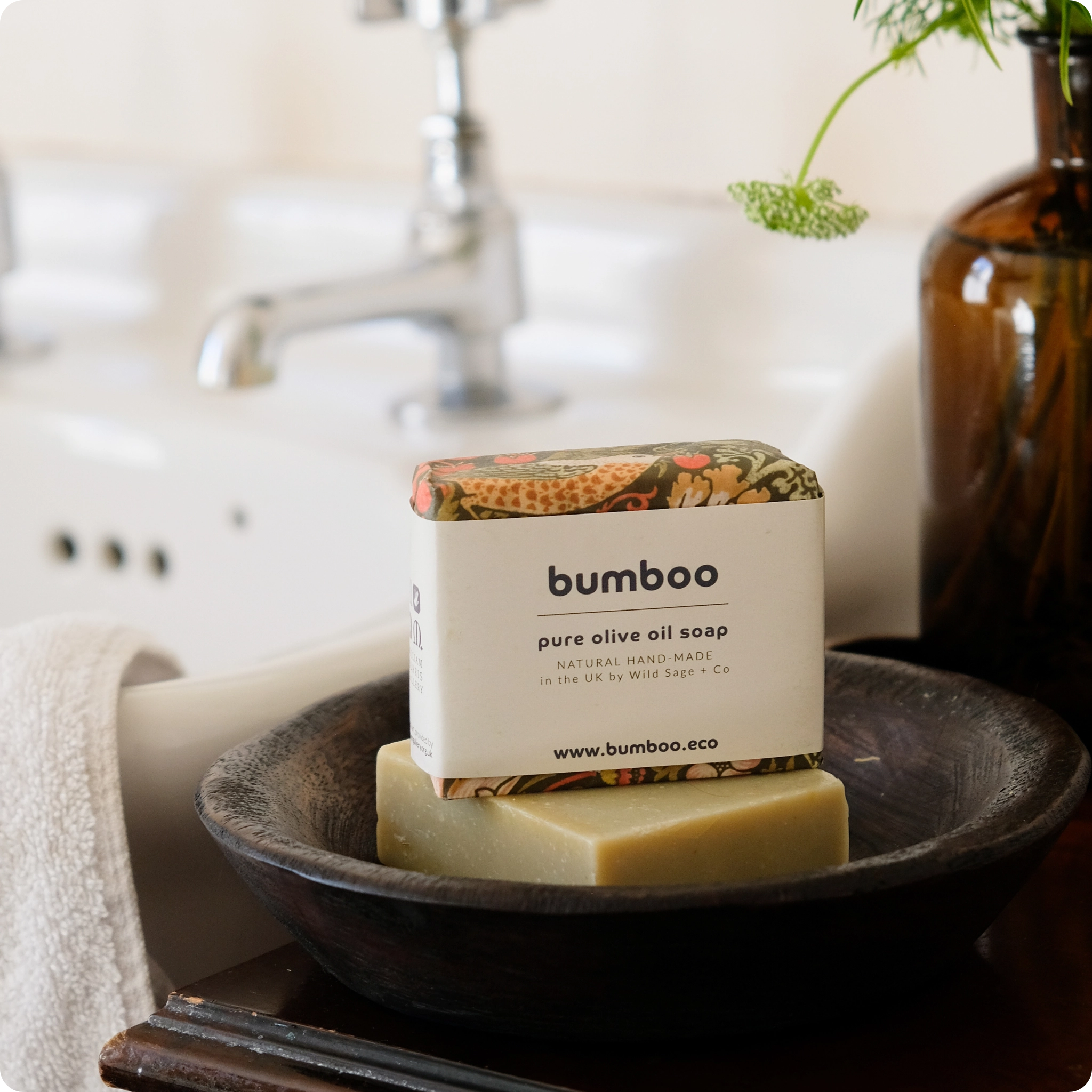 Natural soap wrapped in william morris packaging in a dish next to a bathroom sink.