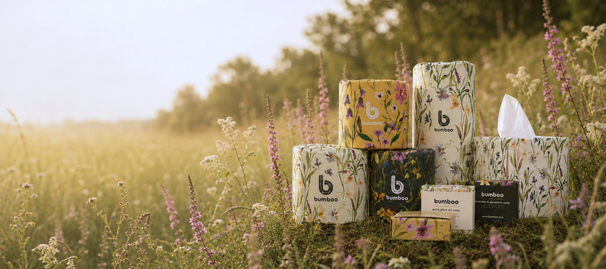 A group of bamboo facial tissue toilet rolls and kitchen rolls in various floral and patterned designs, arranged in a field of wildflowers with a blurred natural background.