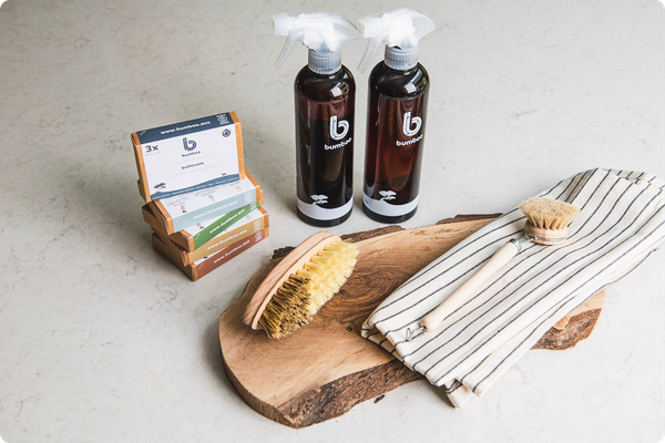 Two bottles of cleaning products on a wooden board with a brush and cloth, on a light background.