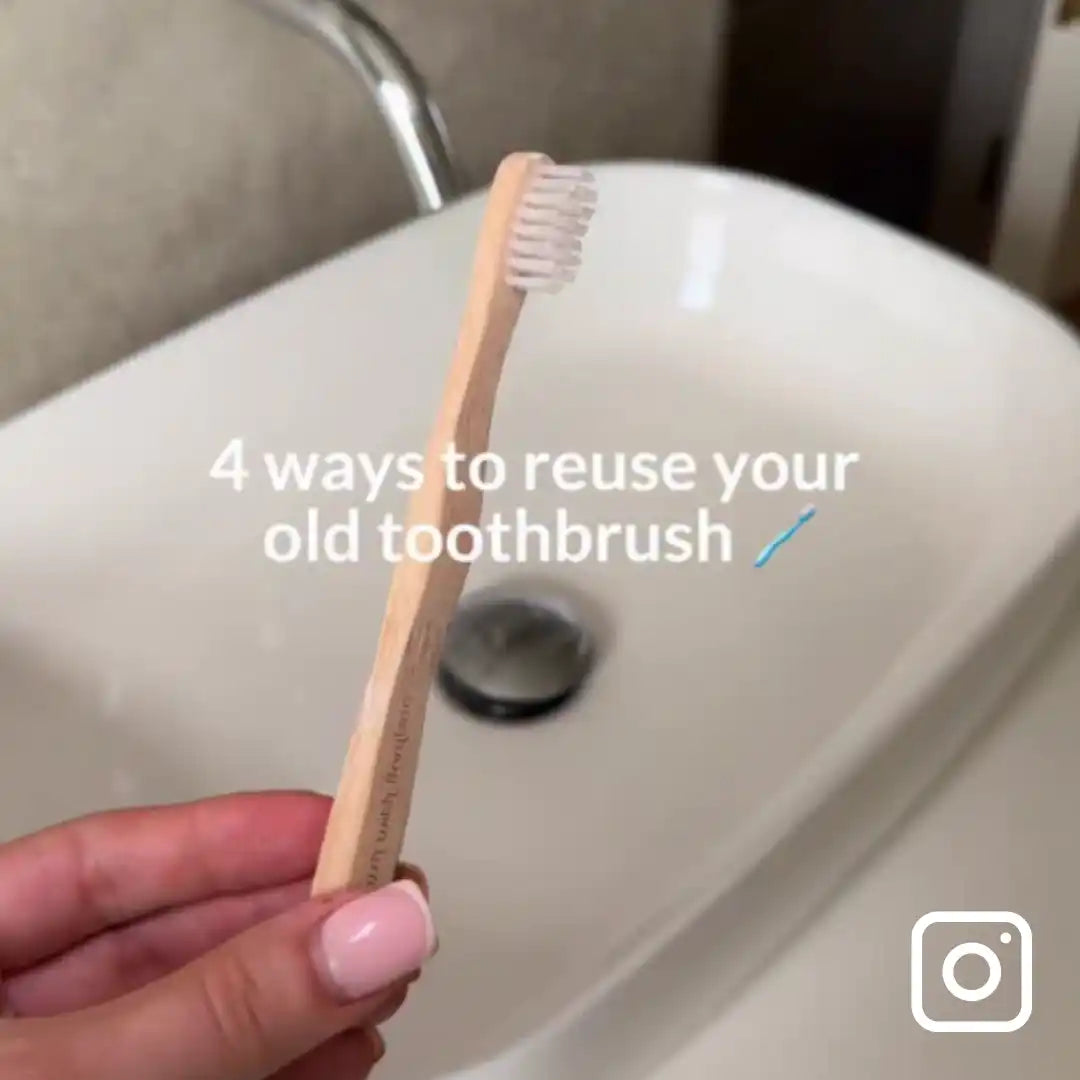 Hand holding a bamboo toothbrush with text overlay '4 ways to reuse your old toothbrush' over a bathroom sink.