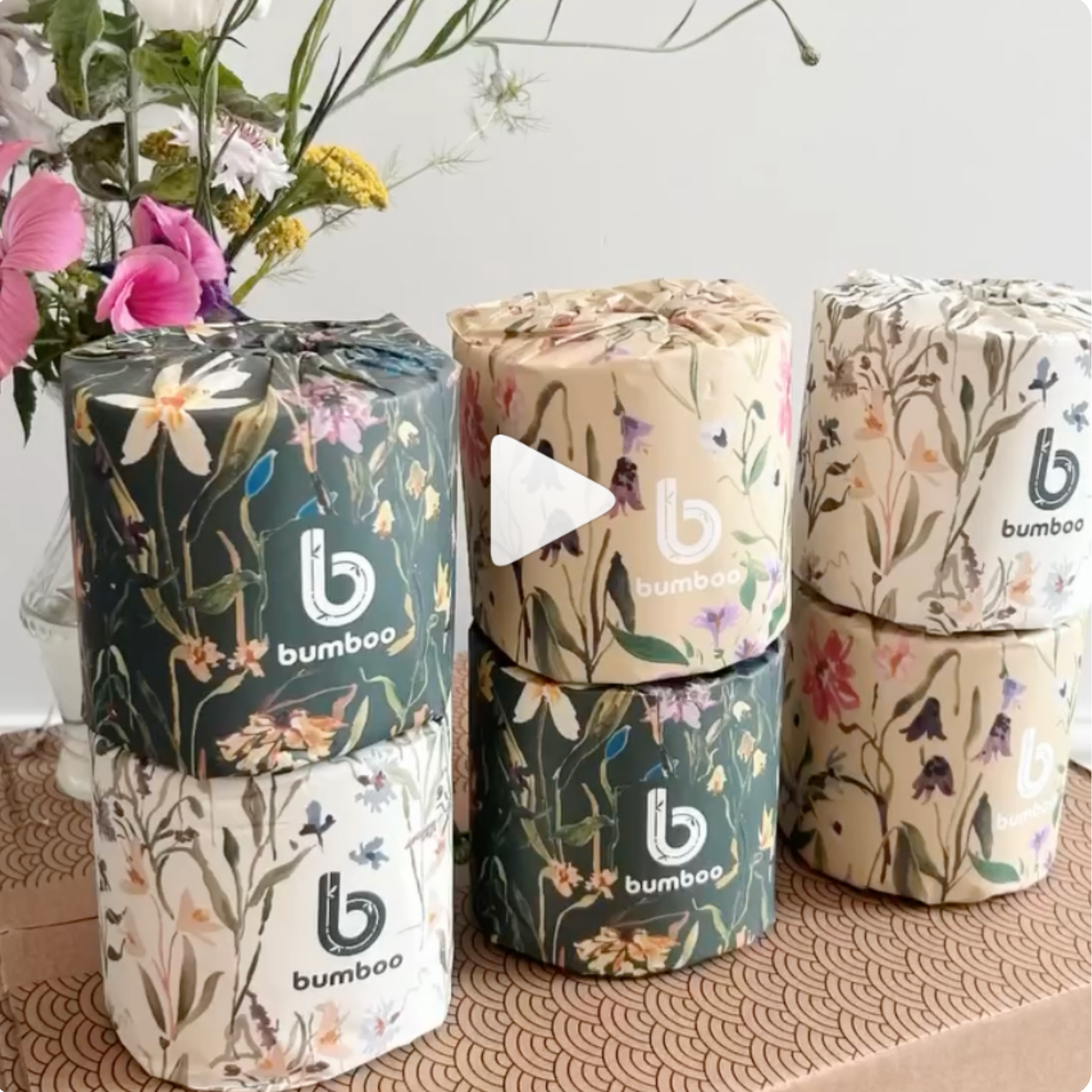 Stack of toilet paper rolls with floral designs and 'bumbo' branding on a textured surface.