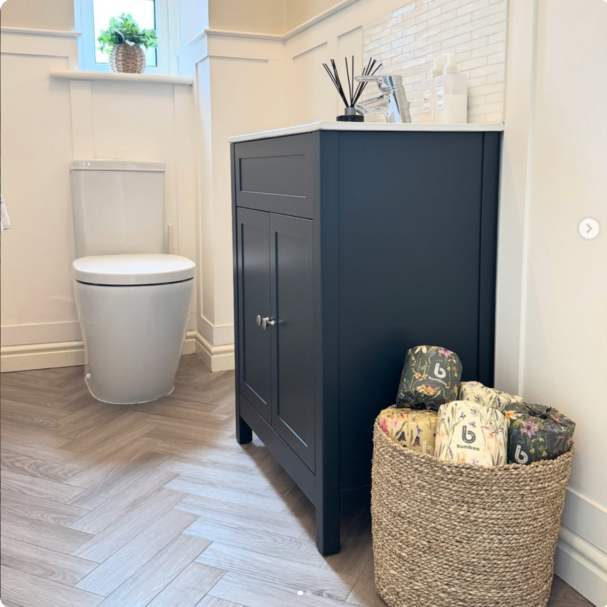 Bathroom with a dark blue vanity unit, white toilet, and decorative items on a wooden floor.